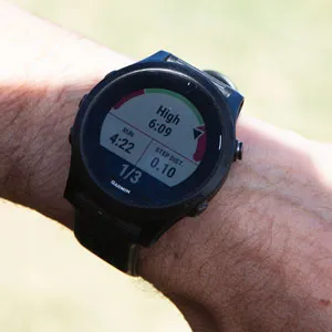 Garmin watch on wrist showing an active workout step with a red speedometer-style gauge reading 'High', a pace of 6:09, and step counter 1 of 3.