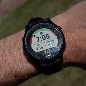 Garmin watch on wrist showing an active workout step with a mostly green gauge, current pace 7:05, step time 4:15, step distance 0.11 miles, step counter 1 of 3.