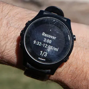 Garmin watch on wrist showing a recovery step with 3:00 remaining, target pace range 9:32 to 12:05 per mile, step counter 1 of 3.