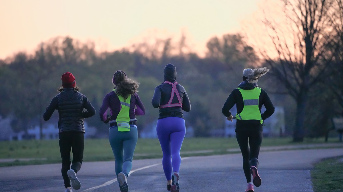Four runners seen from behind, jogging easy on an open road at dawn.