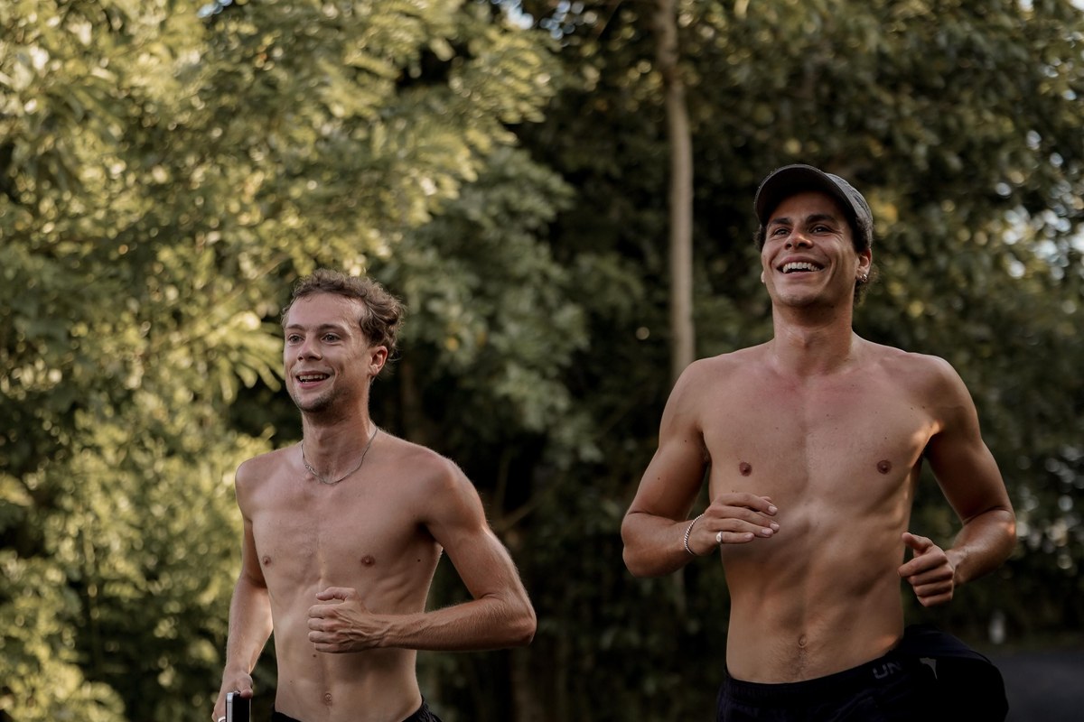 Two distance runners running side by side on a path at an easy, relaxed pace, mid-conversation — one talking, both comfortable, not straining.
