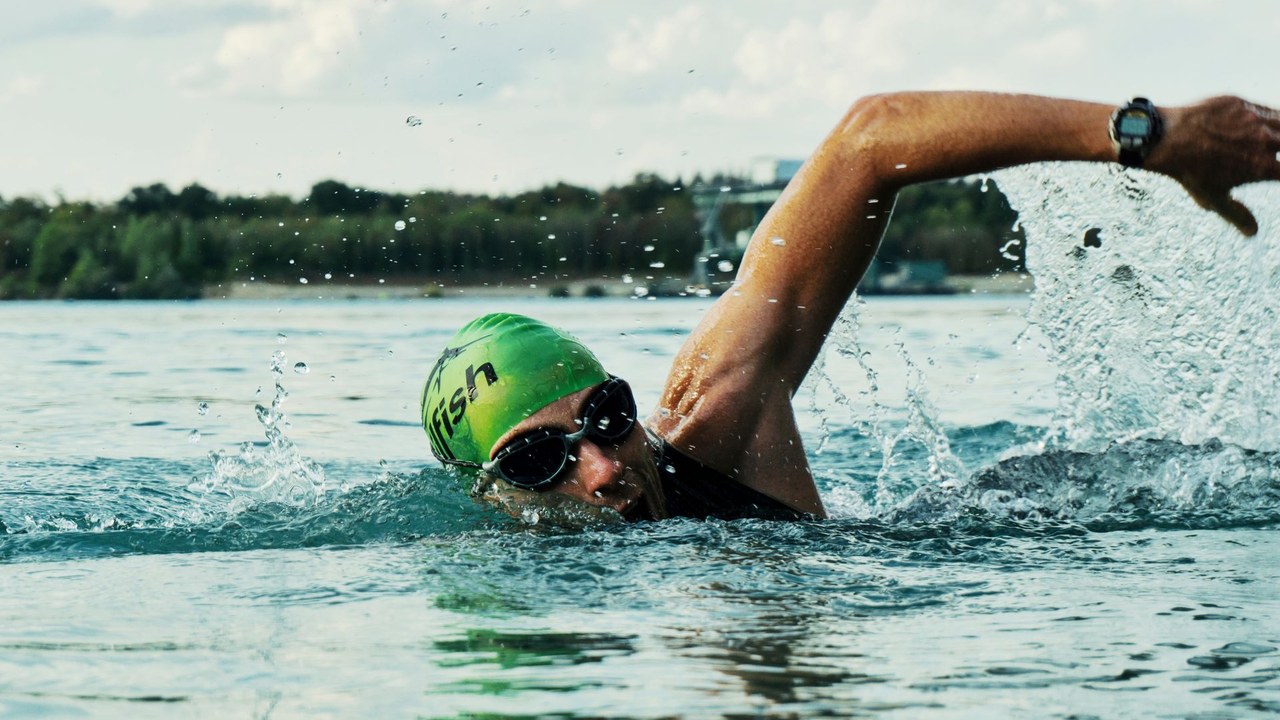 An open-water swimmer mid-freestyle stroke at water level, green cap and goggles.