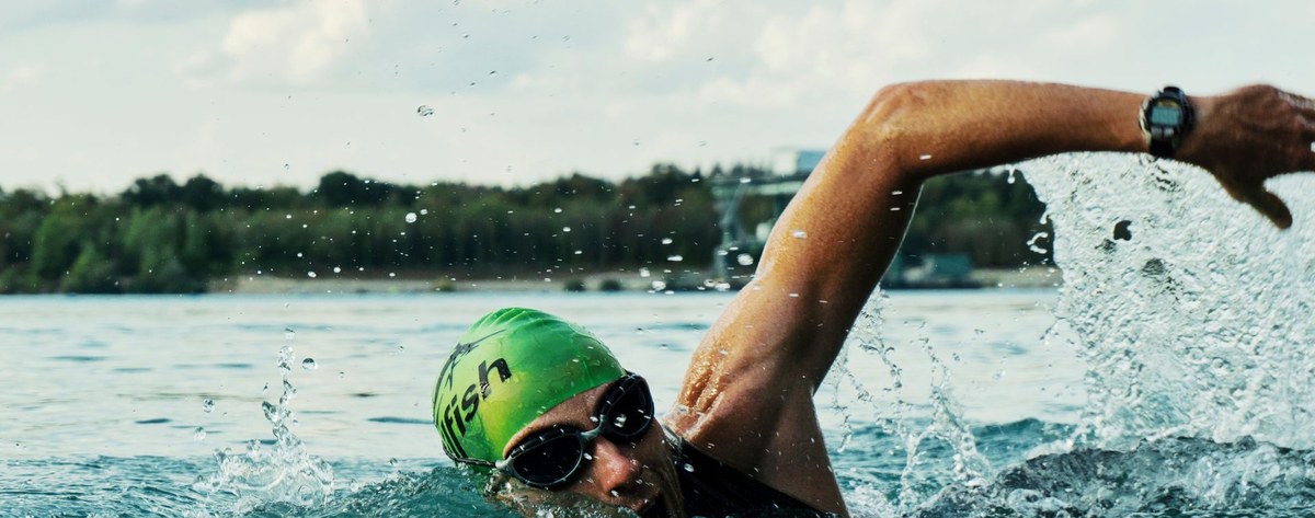 An open-water swimmer mid-freestyle stroke at water level, green cap and goggles.